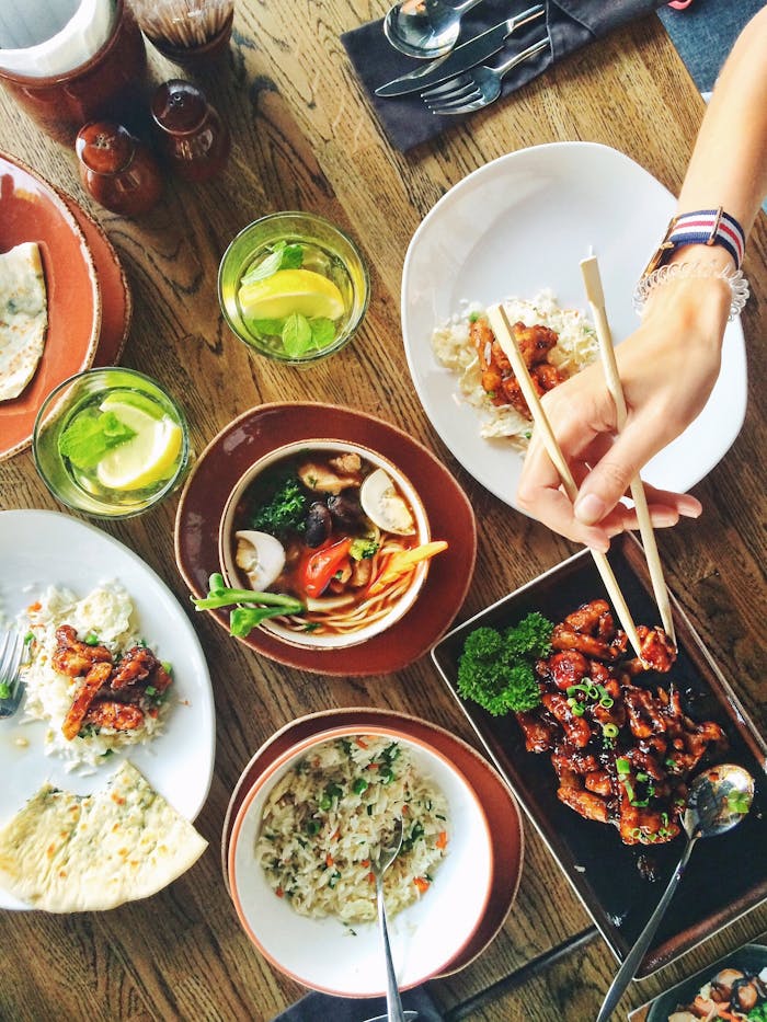 A vibrant display of Asian cuisine with chopsticks, drinks, and diverse dishes on a wooden table.