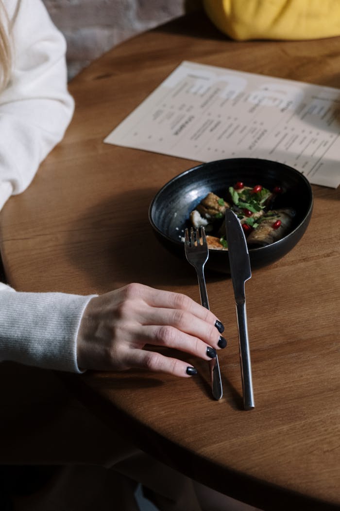 Close-up of a woman's hand with black nails holding cutlery near a restaurant meal.